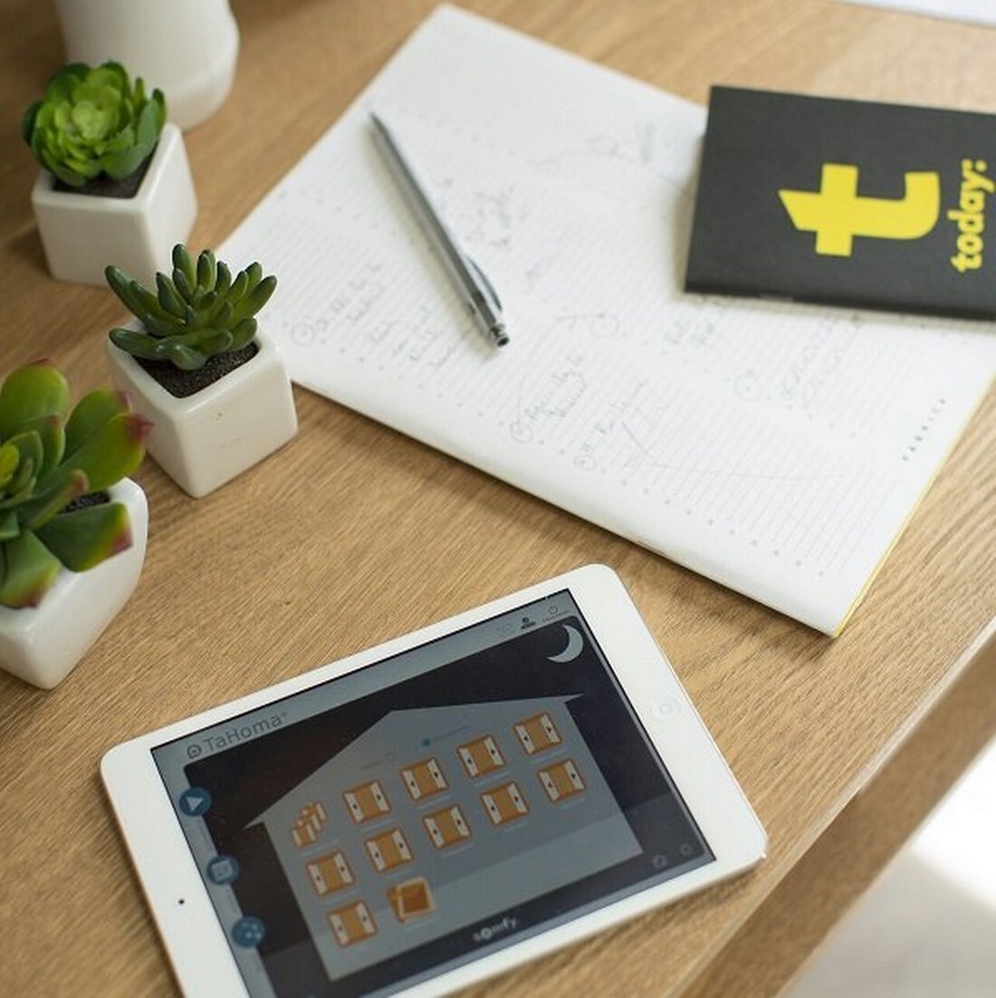 Schreibtisch mit einem Tablet auf dem die Somfy Smart Home TaHoma App geöffnet ist.
